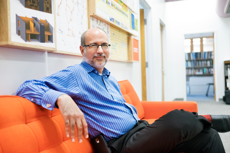 John Poros of MSU&amp;amp;#039;s School of Architecture sitting on an orange sofa.